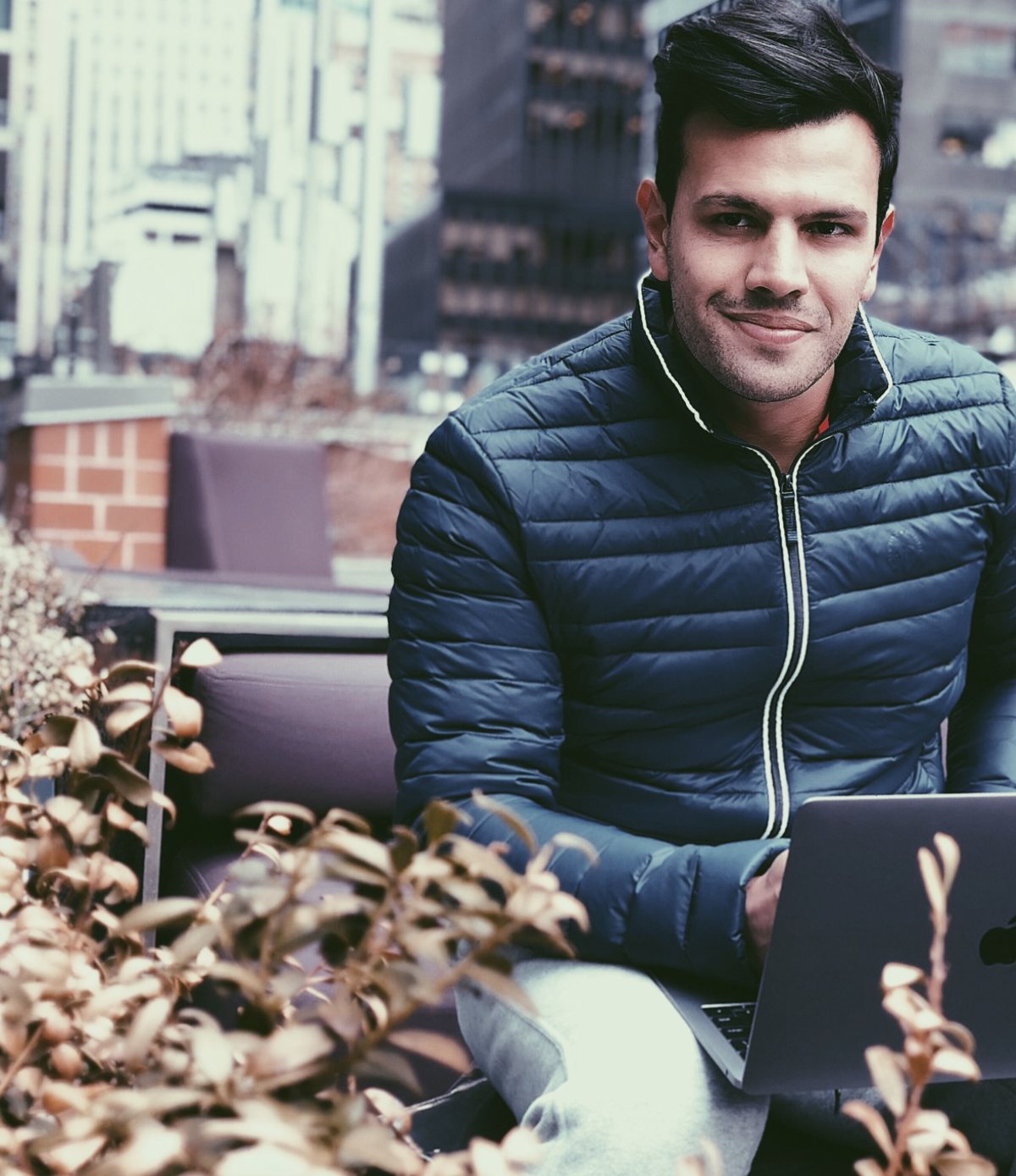 Daniel Malinoski sorrindo, com notebook, num terraço entre prédios