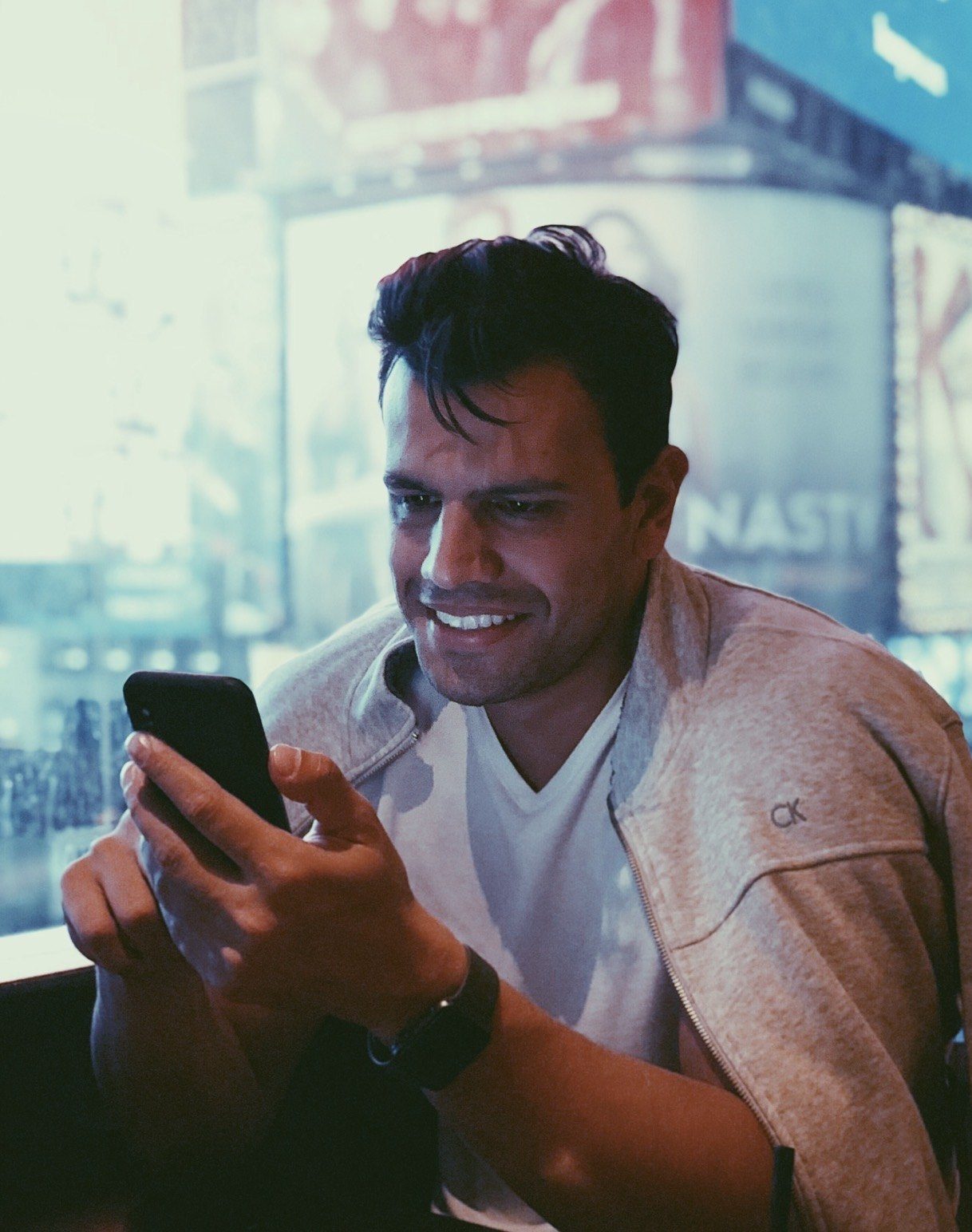 Daniel Malinoski sorrindo enquanto olha o celular, com as luzes da cidade ao fundo
